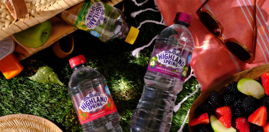 Bottles of Highland Spring flavours water at a picnic with food spilled out onto a patch of grass.