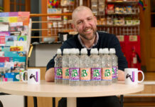 Brad Whittingham, Four Pillars LGBT+ Inclusion Advocate, sits at a table with bottles of MacB water and Four Pillars branded mugs.