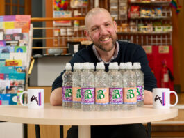 MacB brings a financial boost to Aberdeenshire charities Brad Whittingham, Four Pillars LGBT+ Inclusion Advocate, sits at a table with bottles of MacB water and Four Pillars branded mugs.