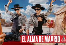 Promotional image for Madri Excepcional 2025 summer campaign with two women working on a DJ set whilst dancing, a person holds a Madri pint glass in the foreground with beer inside the glass.