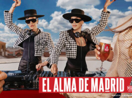 Promotional image for Madri Excepcional 2025 summer campaign with two women working on a DJ set whilst dancing, a person holds a Madri pint glass in the foreground with beer inside the glass.