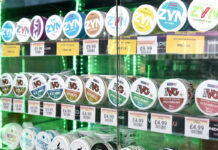 A glass cabinet filled with nicotine pouches that has been backlit with a green light.