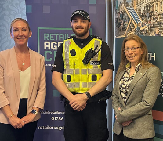 A police officer stands between two women with signage behind them for Retailers Against Crime and Go Forth Stirling.