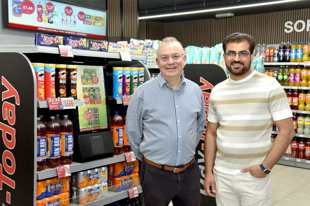 Mike Leonard, symbol director at UWS, and Adeel Iqbal, store owner at Day-Today Anniesland. both stand in front of the UWS promotional touch screen.