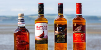 Bottle of The Famous Grouse whisky and The Naked Malt are lined up on a stone wall with an ocean view behind them.