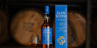 A bottle of Glen Scotia 12 Year Old stands next to its outer box packaging with a dram of the whisky inside a nosing glass next to it. All three stand on top of a barrel.