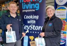 A member of the KeyStore team and a member of the Healthy Living Programme team stand inside a KeyStore shop holding bags as part of a recipe meal initiative with the KeyStore estate.