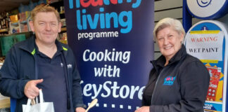 A member of the KeyStore team and a member of the Healthy Living Programme team stand inside a KeyStore shop holding bags as part of a recipe meal initiative with the KeyStore estate.