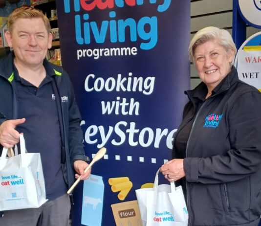 A member of the KeyStore team and a member of the Healthy Living Programme team stand inside a KeyStore shop holding bags as part of a recipe meal initiative with the KeyStore estate.