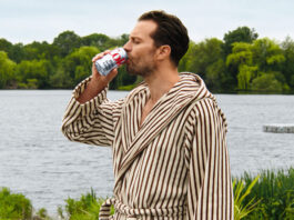 Hollywood actor Jamie Dornan stands in a dressing gown drinking from a can of Diet Coke with a lake behind him.
