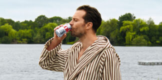 Hollywood actor Jamie Dornan stands in a dressing gown drinking from a can of Diet Coke with a lake behind him.