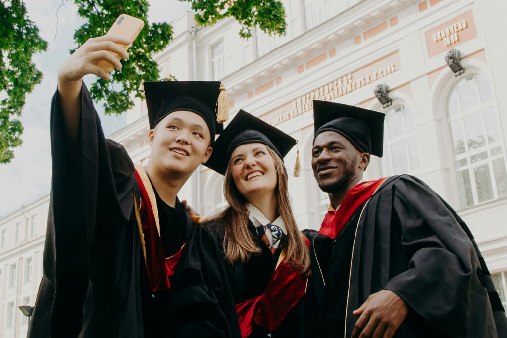 Three university graduates stand together taking a selfie.