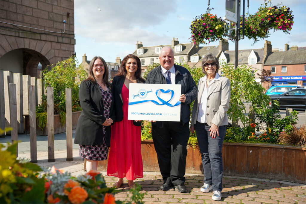 A group of people stand together holding a cheque from Scotland Loves Local.