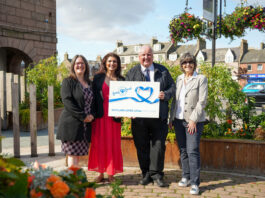 A group of people stand together holding a cheque from Scotland Loves Local.