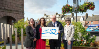 A group of people stand together holding a cheque from Scotland Loves Local.
