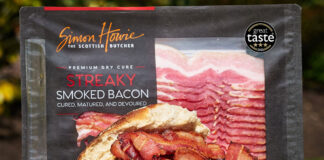 A packet of Simon Howie Smoked Streaky Bacon stands behind a bread roll filled with cooked strips of the bacon with a Three Star Great Taste Award on the packet of bacon.