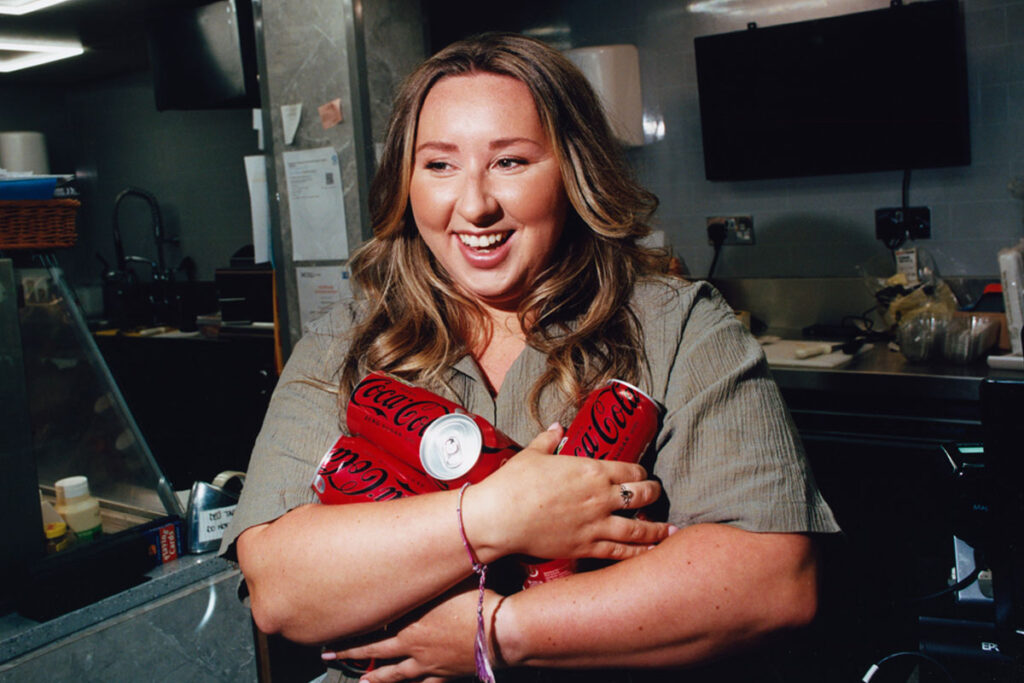 Edinburgh retailer Sophie Williams stands holding cans of Coca-Cola Zero Sugar in her arms.