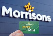 A person holds up a Morrisons More card against a Morrisons sign which is on a building with black panelling.