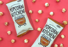Packets of Popcorn Kitchen Gingerbread Popcorn lie against a red background with pieces of the popcorn dotted around them.