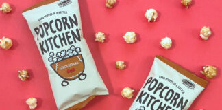 Packets of Popcorn Kitchen Gingerbread Popcorn lie against a red background with pieces of the popcorn dotted around them.
