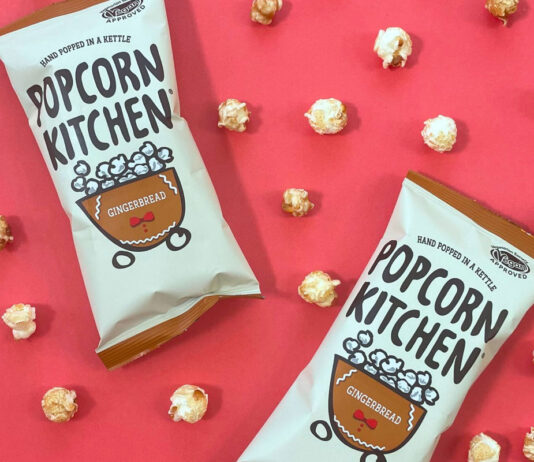 Packets of Popcorn Kitchen Gingerbread Popcorn lie against a red background with pieces of the popcorn dotted around them.