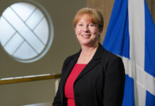 Scottish finance secretary Shona Robison stands in Parliament with the Scotland flag behind her.