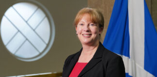Scottish finance secretary Shona Robison stands in Parliament with the Scotland flag behind her.