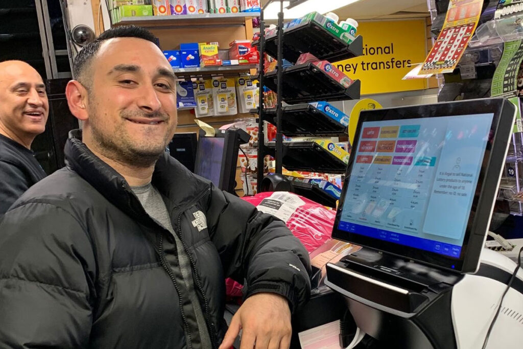 A retailers stands next to an Allwyn The National Lottery Wave terminal in his store.