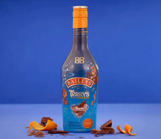 Baileys teams up with Terry’s Chocolate Orange for indulgent Christmas treat A bottle of Baileys Terry's Chocolate Orange limited edition flavour stands in front of a blue background with orange peel and pieces of chocolate around the bottle.