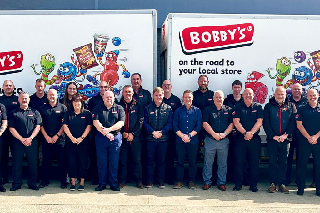 A group of representatives from food supplier Bobby's stand in front of two Bobby's branded vans.