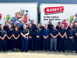 Allwyn strengthens support with Bobby’s partnership A group of representatives from food supplier Bobby's stand in front of two Bobby's branded vans.