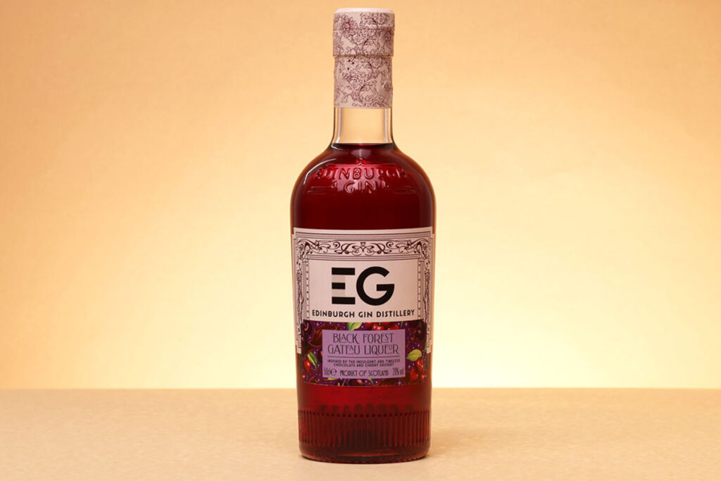 A bottle of Edinburgh Gin Black Forest Gateau Liqueur stands against a lit up background.