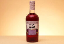 A bottle of Edinburgh Gin Black Forest Gateau Liqueur stands against a lit up background.
