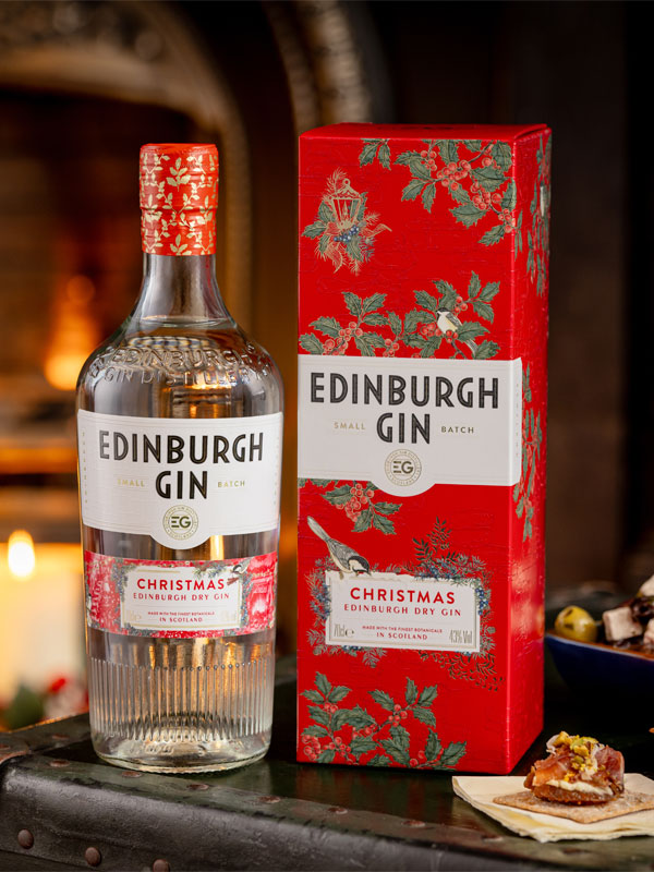 A bottle and box of Edinburgh Gin Christmas Gin stands on a table with a fireplace in the background.
