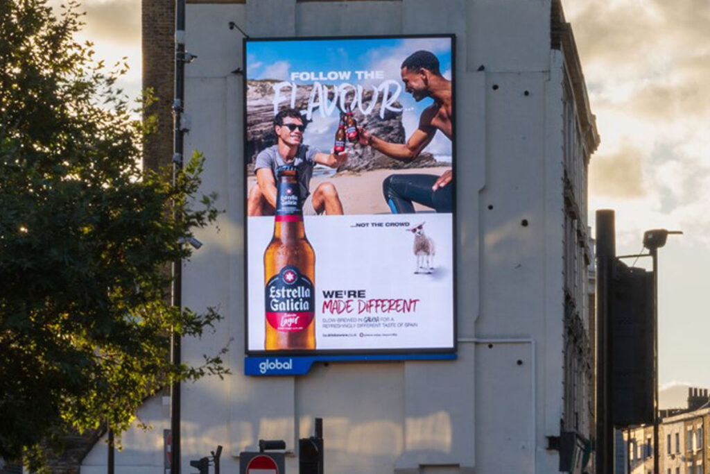 An electronic billboard on the side of a building has the winter 2025 campaign for Estrella Galicia on it.