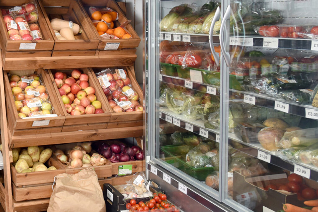 Fruit and veg stalls in a shop as well as a chiller filled with products.