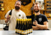 Hive Mind and Rave Coffee team up on new Stout Team members from Hive Mind brewery and Rave Coffee stand together hold bottles of a new brew which the two firms collaborated on. There are bottle of the drink on the table in front of them.