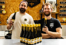 Team members from Hive Mind brewery and Rave Coffee stand together hold bottles of a new brew which the two firms collaborated on. There are bottle of the drink on the table in front of them.