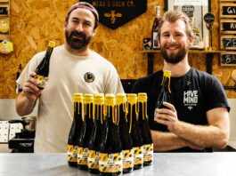 Team members from Hive Mind brewery and Rave Coffee stand together hold bottles of a new brew which the two firms collaborated on. There are bottle of the drink on the table in front of them.