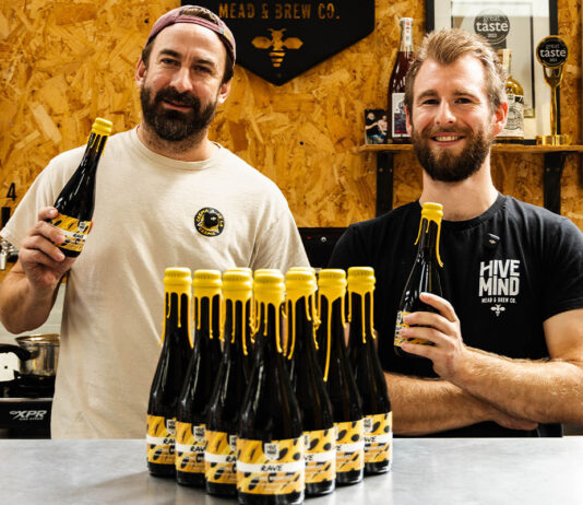 Hive Mind and Rave Coffee team up on new Stout Team members from Hive Mind brewery and Rave Coffee stand together hold bottles of a new brew which the two firms collaborated on. There are bottle of the drink on the table in front of them.