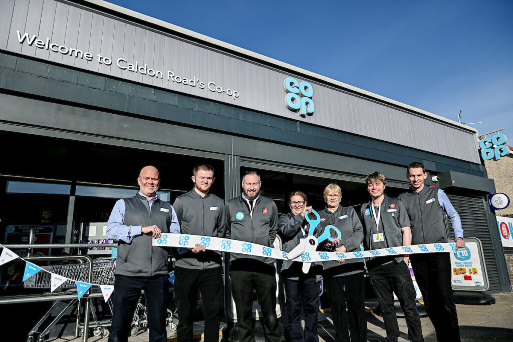 Staff at the Co-op Caldon Road Store stand in front of the shop with a novelty pair of scissors and ribbon to mark the completion of its refit.