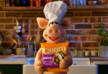 A puppet pig wearing a chef hat stands in a kitchen holding a bag of Quorn Mince.
