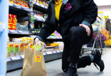 A man is packing a paper bag with groceries with the Scoot logo on the bag. The man is also wearing some Scoot branded clothing.