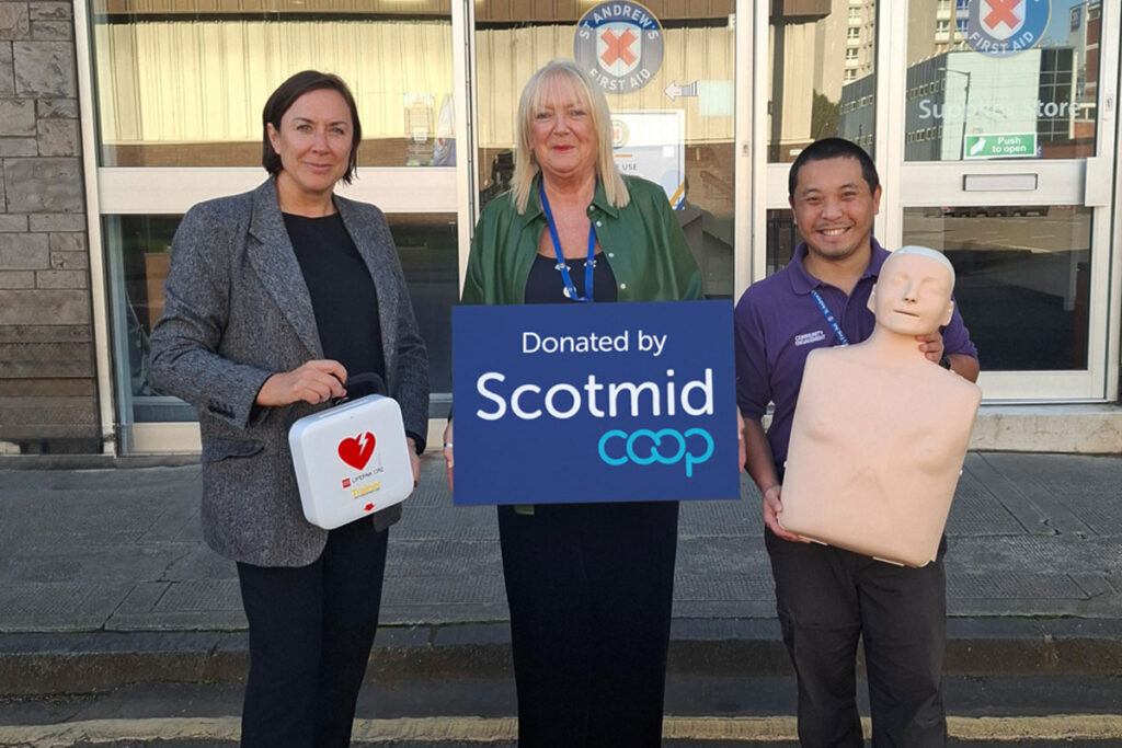 Lynne Ogg, head of membership & community engagement at Scotmid, stands holding a first aid kit next to Moyra Reid, head of marketing, communications and fundraising at St Andrew's First Aid and Daniel Handy. Moyra holds a placard with the Scotmid Co-op logo on it and Daniel holds a dummy used to perform CPR on.