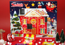 The Swizzels Advent Calendar for 2025 stands against a red background with packets of Swizzels sweets lying in front of the calendar. Doors one the calendar have also been opened.