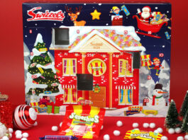 The Swizzels Advent Calendar for 2025 stands against a red background with packets of Swizzels sweets lying in front of the calendar. Doors one the calendar have also been opened.