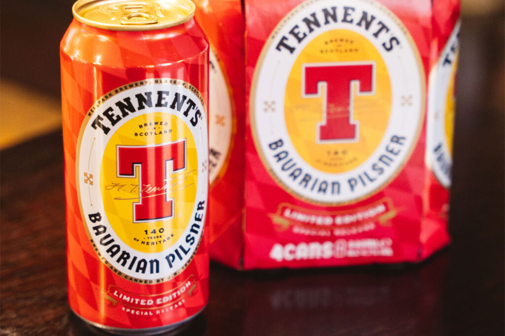 A can of Tennent's Bavarian Pilsner stands next to a four-pack of the beer on a table.