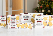Packs of Walker's Shortbread 2025 Christmas selection stand upright on a white marble table with a Christmas tree in the background.