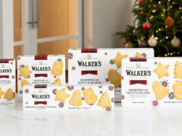 Packs of Walker's Shortbread 2025 Christmas selection stand upright on a white marble table with a Christmas tree in the background.