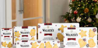 Packs of Walker's Shortbread 2025 Christmas selection stand upright on a white marble table with a Christmas tree in the background.